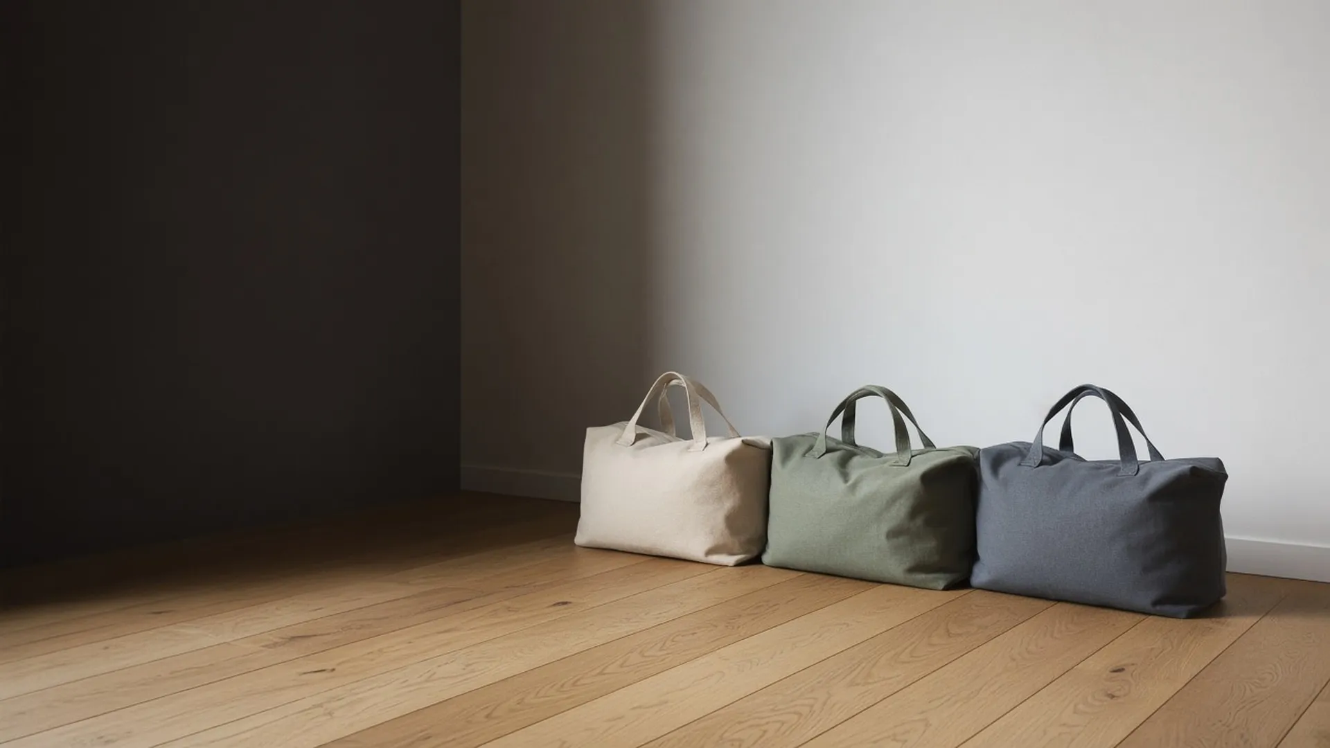Three packed soft bags in oat, sage, and slate grey on an oak floor