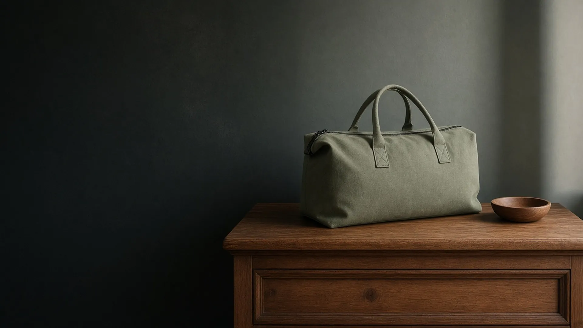 A zipped soft bag on a wooden dresser beside a small empty wooden dish
