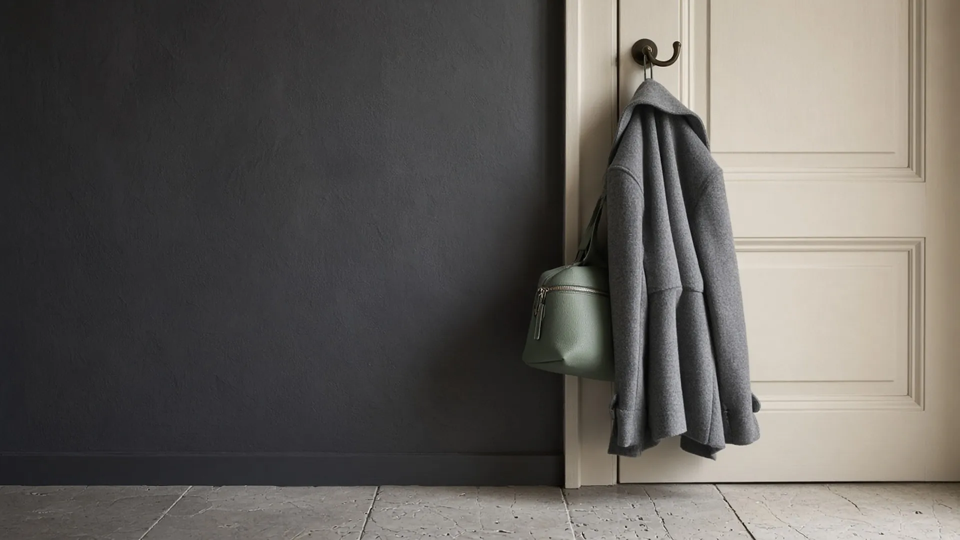 A small zipped sage bag hanging on a hook beside a coat by a door