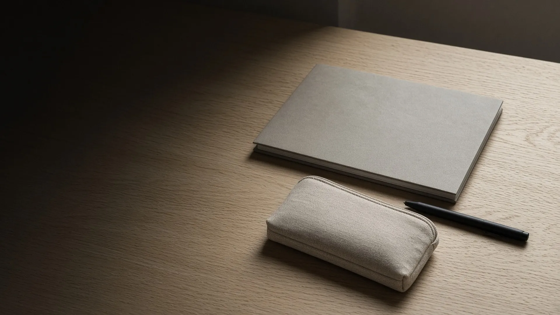 A closed document folder and a zip pouch beside a pen on an oak desk
