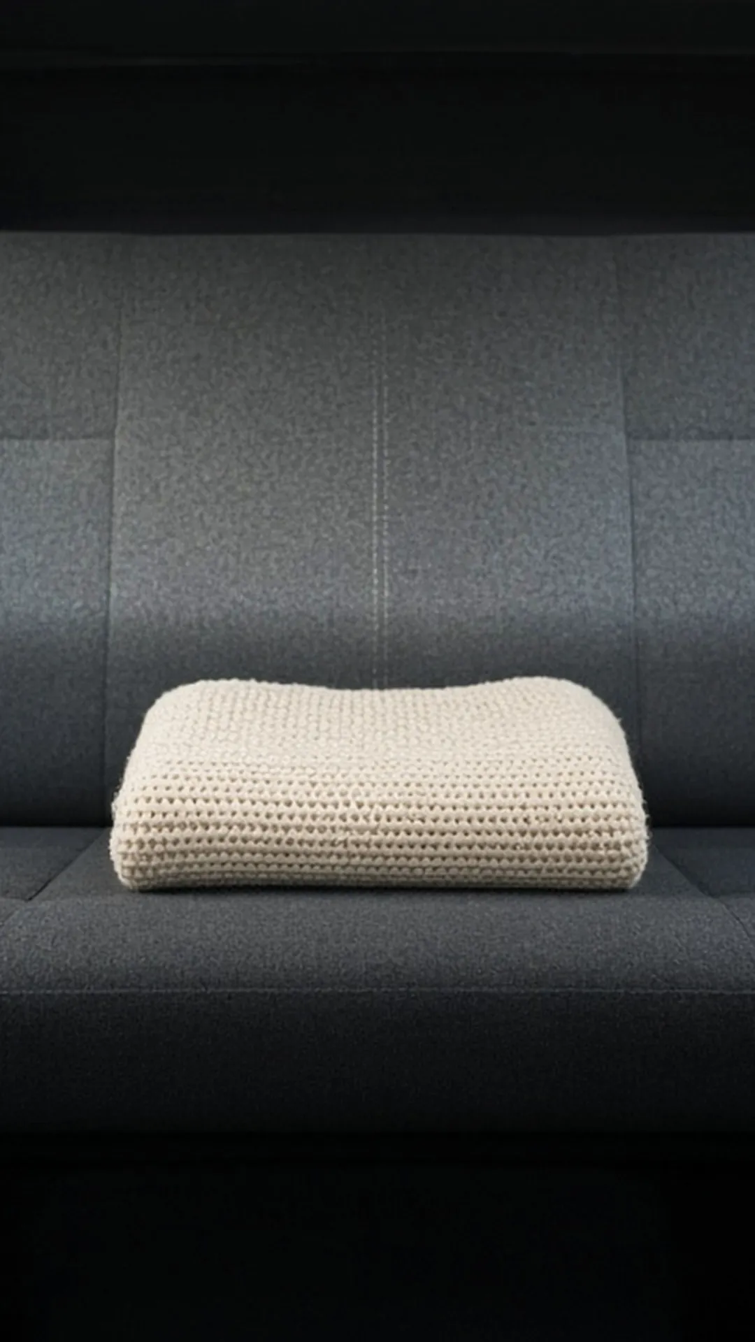 An empty car back seat with grey upholstery and a folded cream blanket