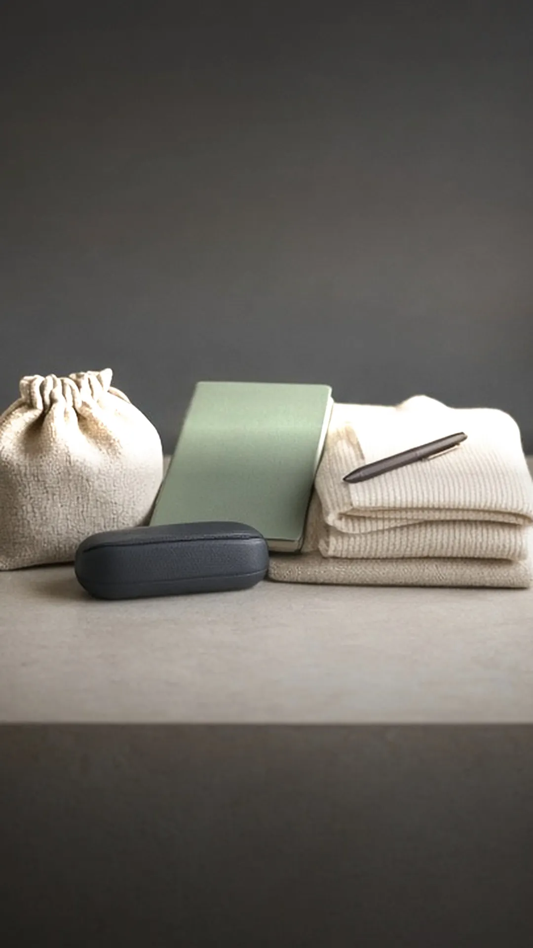 A small bag, a glasses case, a closed folder, and a cardigan on a table