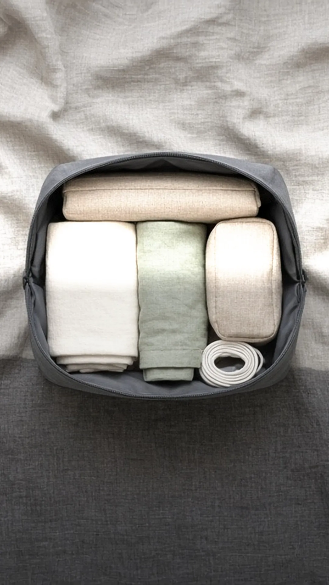 An open bag from above packed in neat sections with pouches, clothes, and a cable