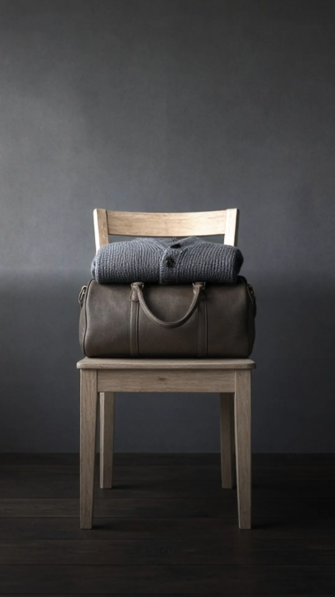 A packed brown duffel bag with a folded grey cardigan on a pale wooden chair